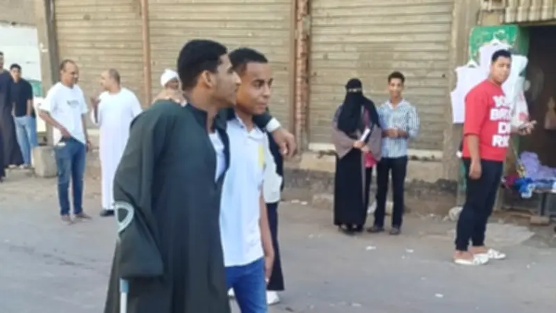 طالب يساند صديقه على عكاز أثناء دخول لجنة الثانوية العامة بقنا